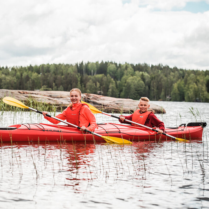 Kesäleirillä tyttö ja poika melomassa kajakilla