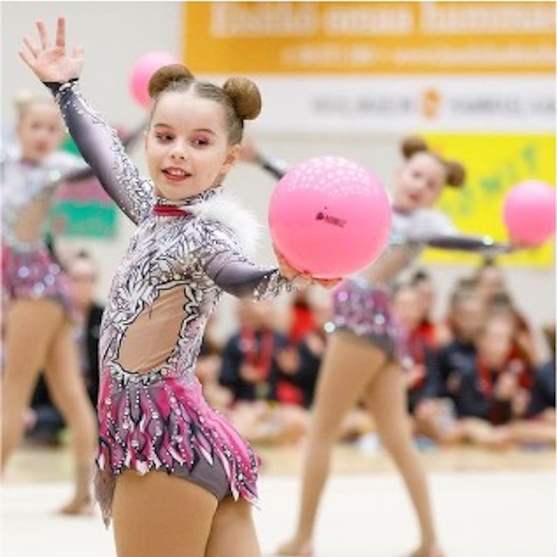 Valmentajaseminaari. Voimistelijatyttö katsoo taivutuksessa kädessään olevaa palloa.