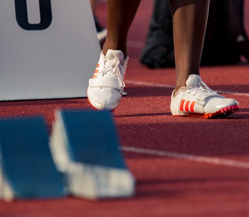 Yleisurheilukentällä lähtötelineiden vieressä yksi ihiminen, josta kuvassa näkyy vain sääret.