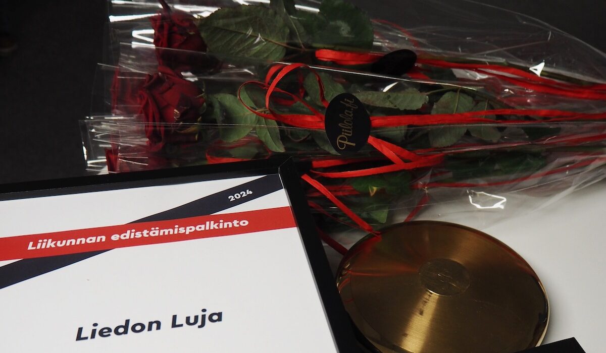 TUL:n päivän palkintoja, kuten ruusuja, kultainen kiekko sekä palkintodiplomi pöydällä.