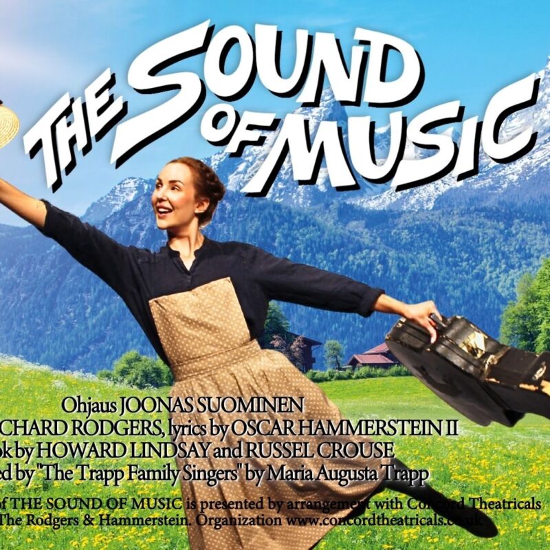 Nainen tanssii hattu ja kitaralaukku kädessään. Taustalla alppimaisema.