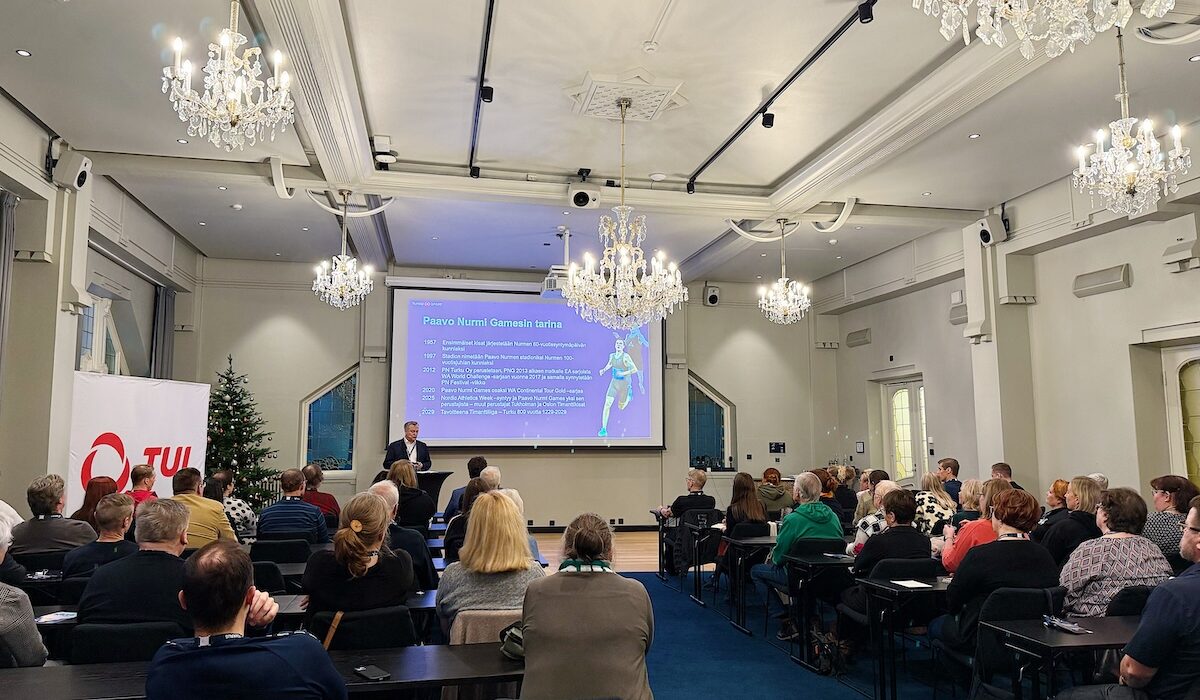 TUL:n Seurapäivien 29.11.2025 yleisöä kuvattuna selkäpuolelta. Etualalla Jari Salonen pitää puheenvuoroa Paavo Nurmi Games -tapahtumakonseptista.