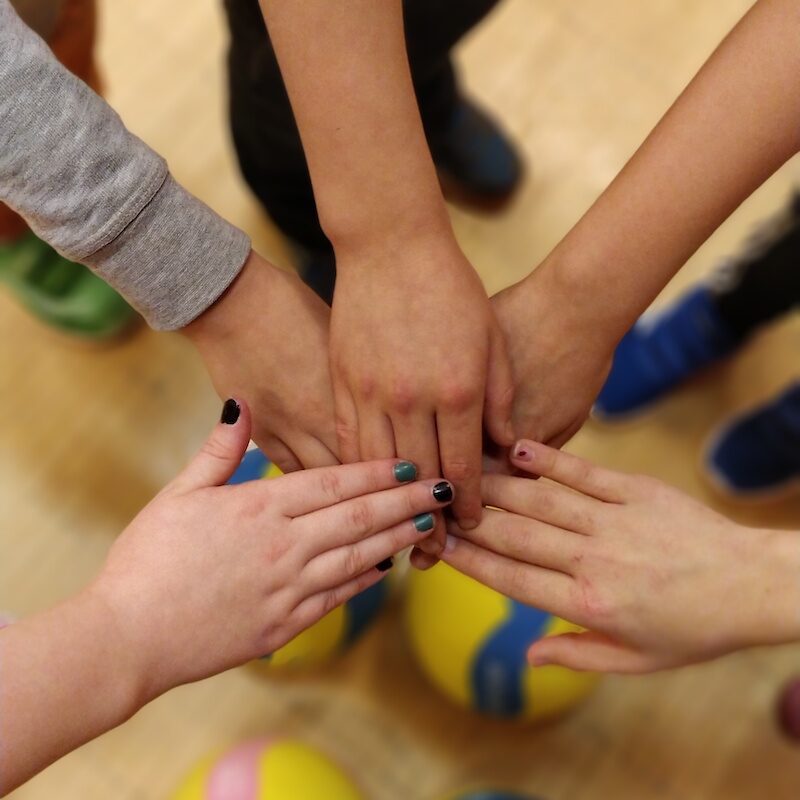 Kädet yhdessä kasassa. Lentopallo käsien alla.