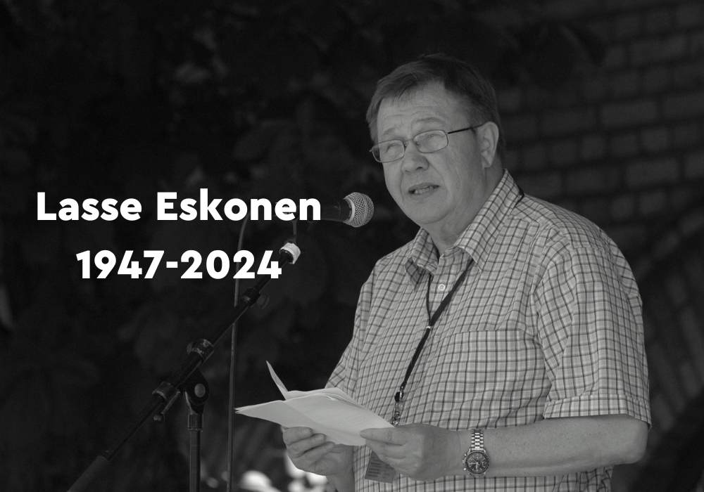 Lasse Eskonen pitämässä puhetta mustavalkoisessa valokuvassa. Lisäksi teksti Lasse Eskonen 1947-2024.