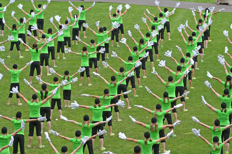 Kuvassa useita voimistelijoita vihreissä paidoissa jalkapallokentällä kädet levitettynä