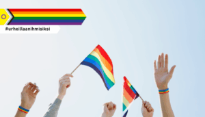 Käsiä ilmassa sateenkaaren väristen Pride-lippujen kanssa. Ylälaidassa nuolen muodossa oleva Pride-tunnus, jonka alapuolella teksti #urheillaanihmisiksi.