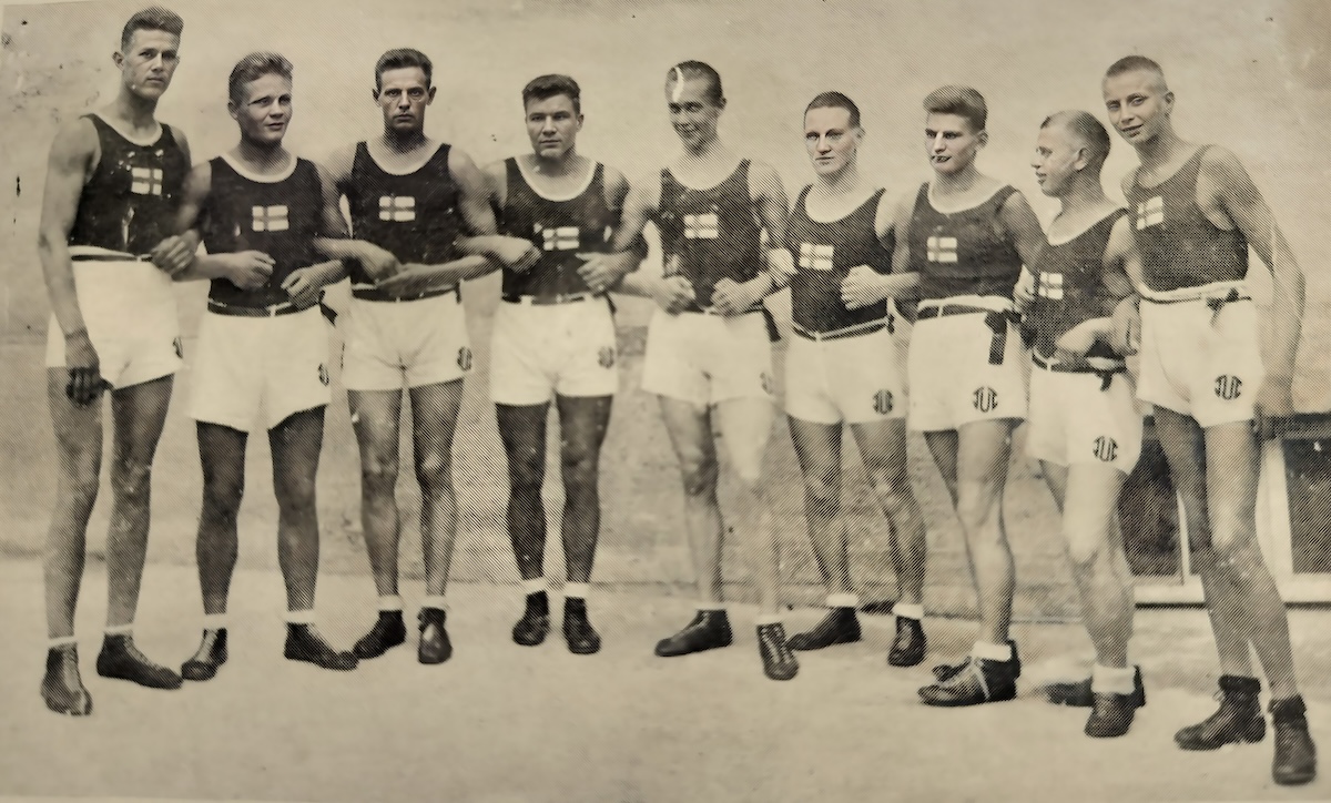 Mustavalkoinen kuva vuodelta 1925. Kuvassa on TUL:n urheilijoita Frankfurt Am Mainin työläisolympialaisissa. Heillä on päällään hihattomat paidat, joissa on Suomen lippu ja valkoiset sortsit, joissa on TUL:n vanha logo.