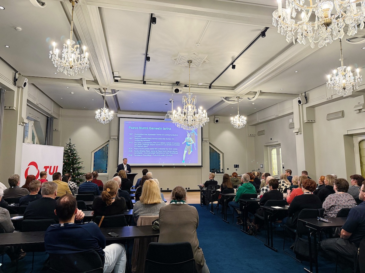 TUL:n Seurapäivien 29.11.2025 yleisöä kuvattuna selkäpuolelta. Etualalla Jari Salonen pitää puheenvuoroa Paavo Nurmi Games -tapahtumakonseptista.